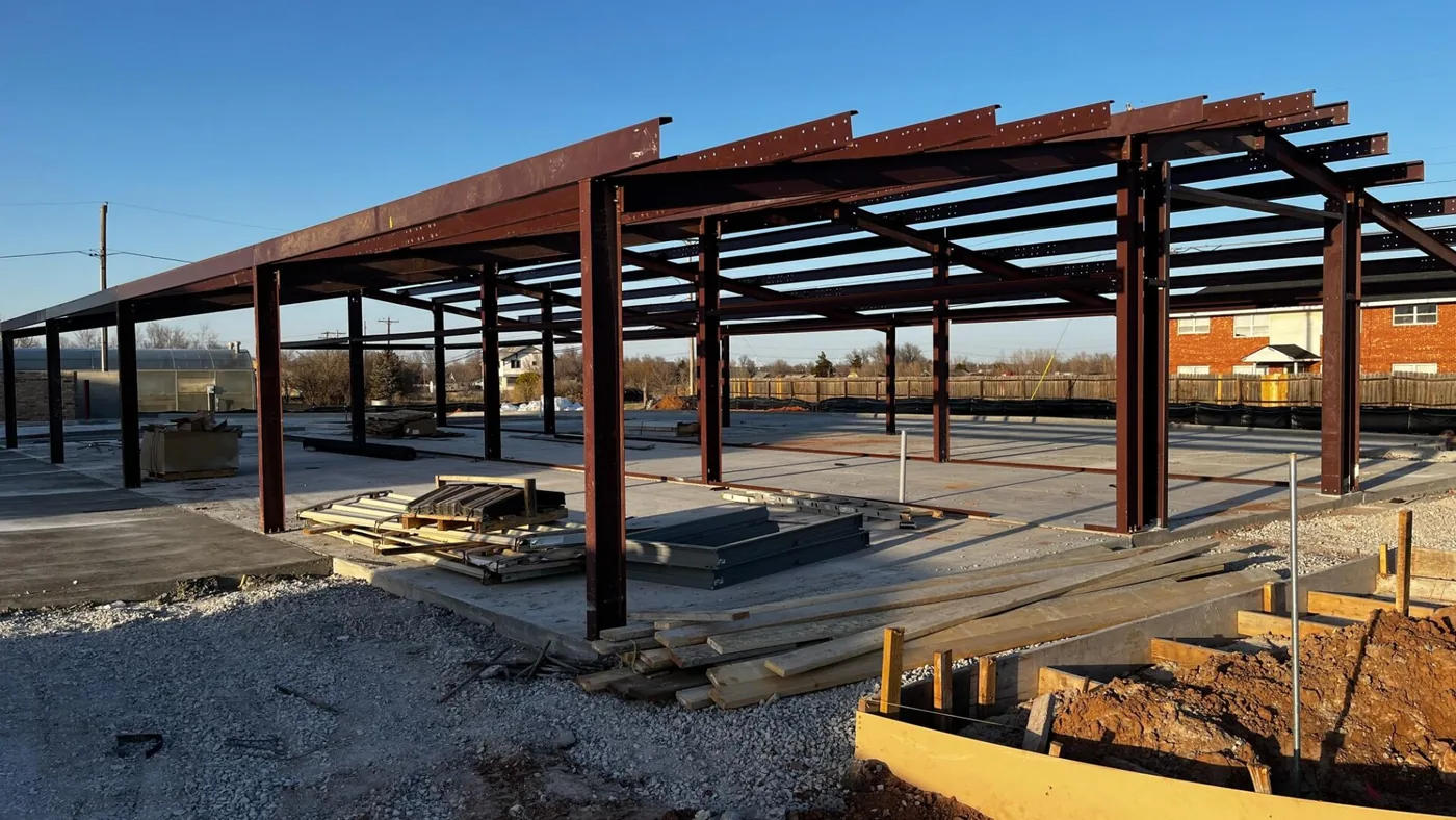 Red steel frame of a commercial building erected on a poured concrete slab at a construction site.
