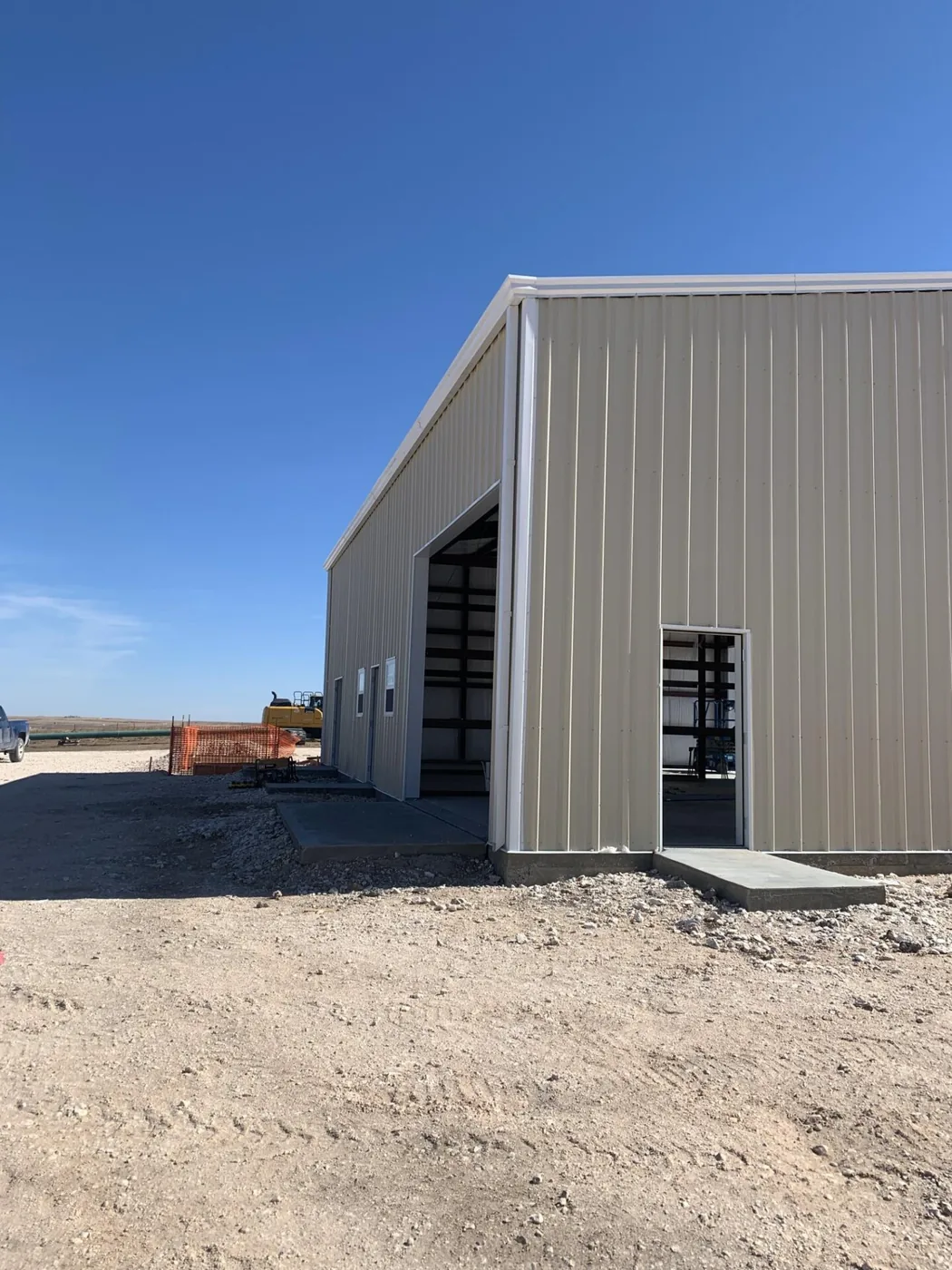 Grey steel shop with two roll-up bay doors and a walk-in door under a clear blue sky
