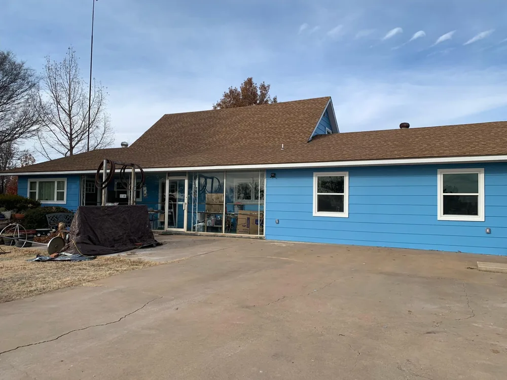 Rear of a blue house with new siding, sliding glass doors and a concrete patio