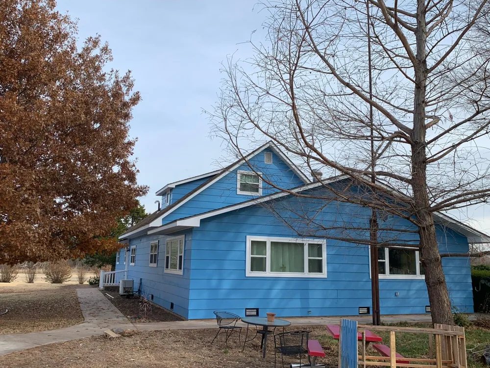 Blue-painted farmhouse with a patio and bare winter trees after exterior work