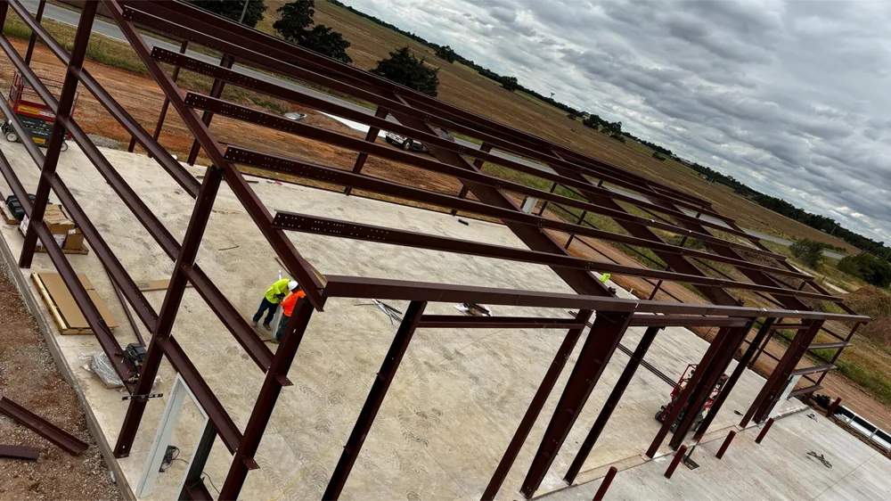 Steel roof purlins going into place with a crew member in a hi-vis vest working below
