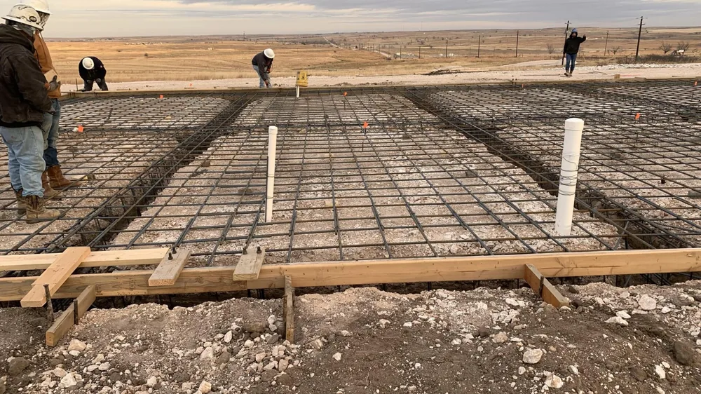 Crew laying out rebar across a large slab form on a windswept lot