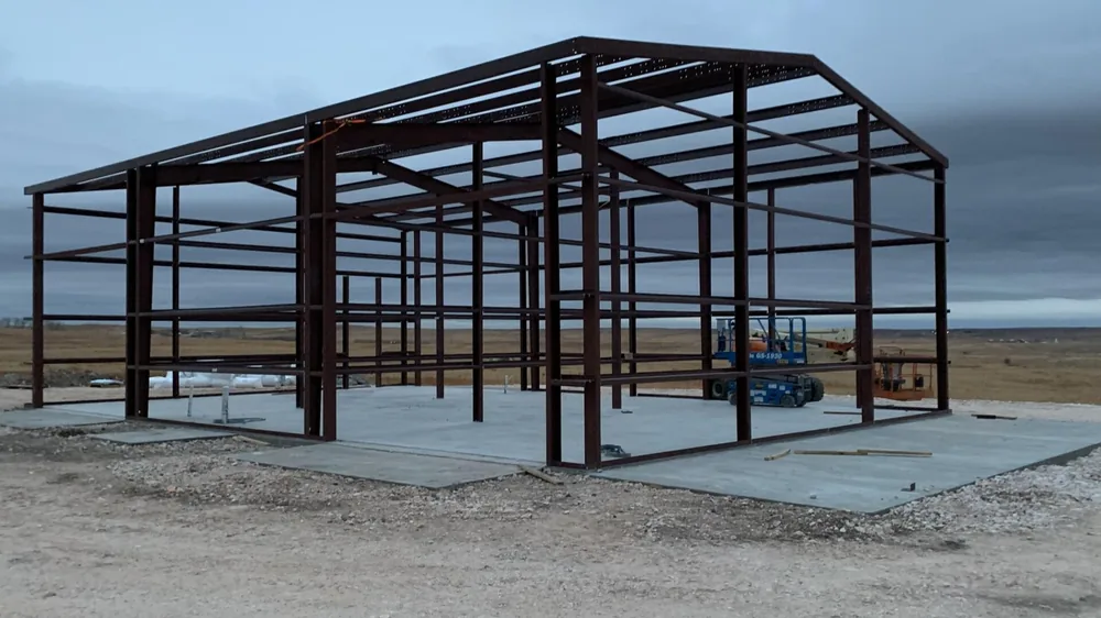 Dark red steel building frame standing on a finished slab under overcast skies