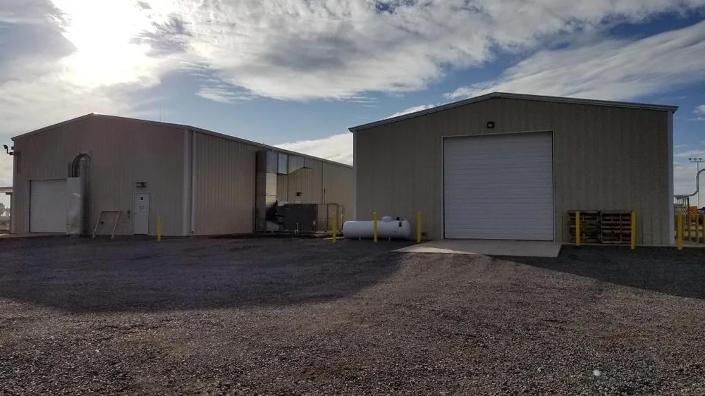 Two tan metal commercial buildings with a white overhead door and a gravel yard