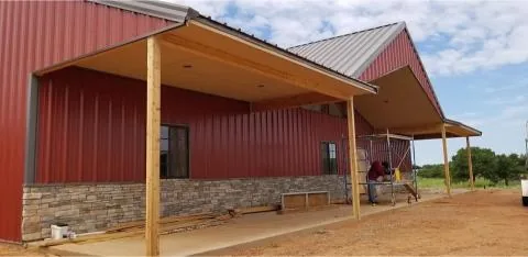 Side of the same red metal barn showing the covered porch and stone wainscot
