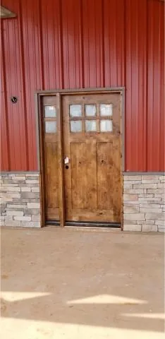 Stained wood front door and sidelight set into a red metal wall above stone veneer