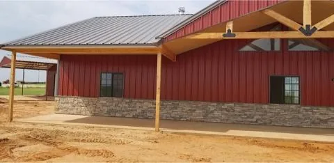 Red barndominium with stone wainscot, cedar porch posts and a metal roof