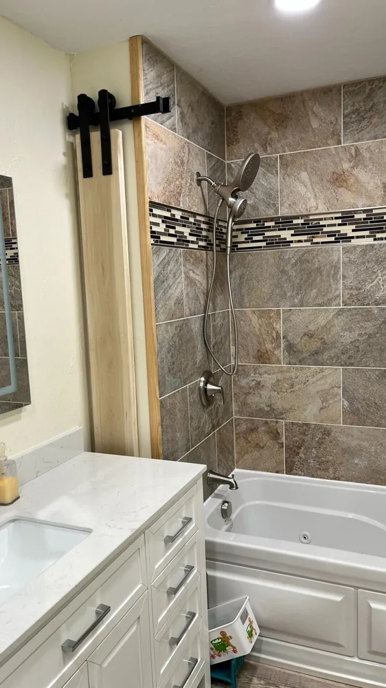 Remodelled bathroom with a tiled tub surround, mosaic accent band and new vanity