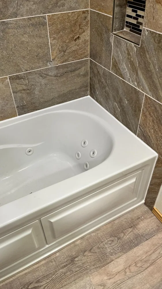 New white soaking tub fitted against a tiled wall over wood-look flooring