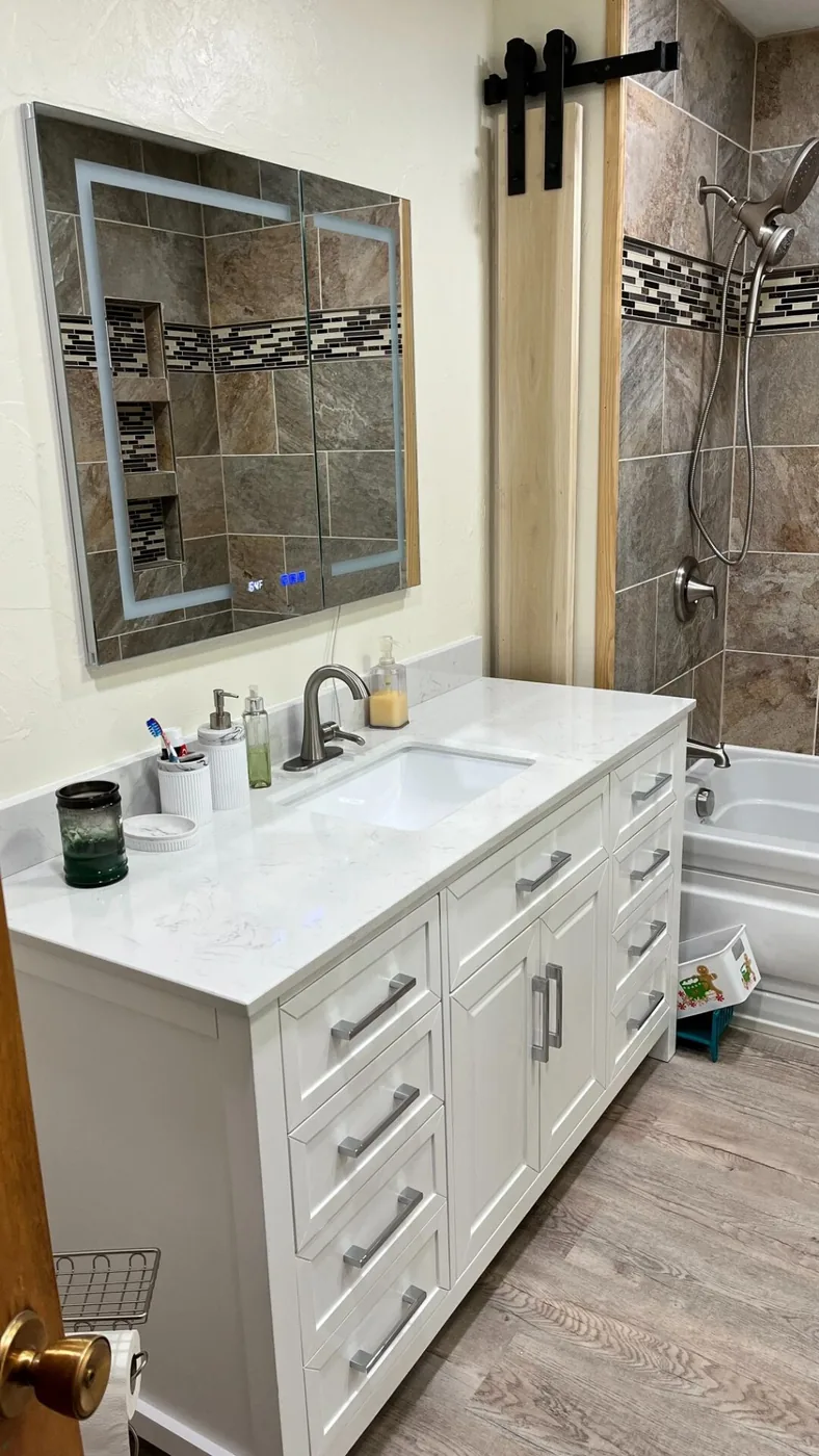 Remodelled bathroom with a white vanity, quartz countertop and tiled tub surround