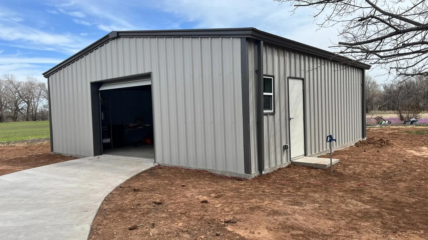 Finished grey steel garage with a roll-up door, walk-in door and new concrete driveway