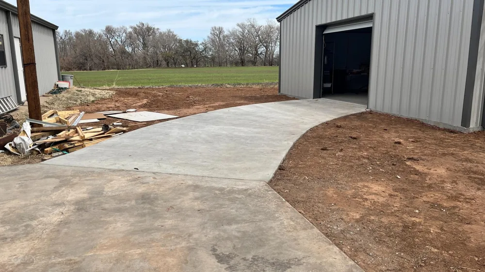New concrete drive curving up to the open overhead door of a grey steel building