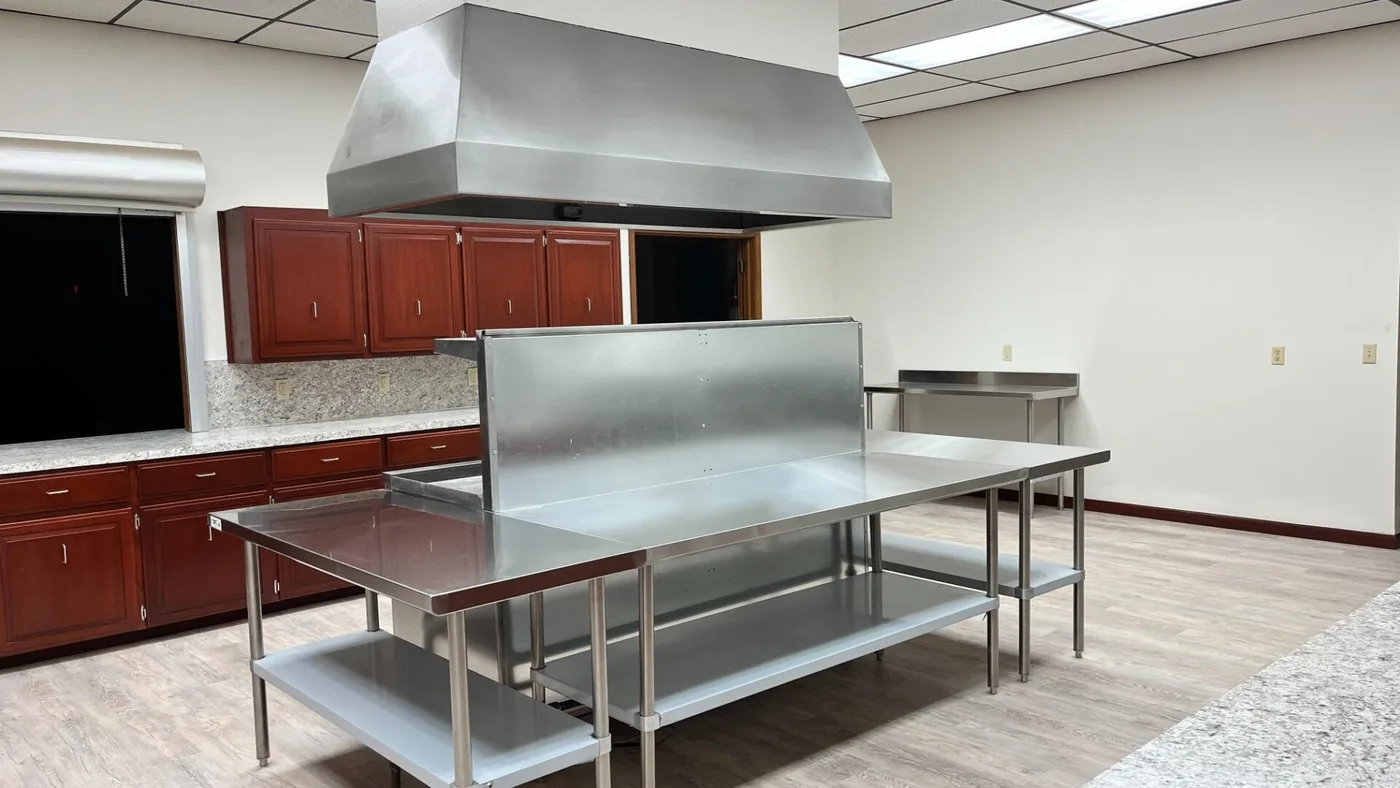 Finished commercial kitchen with newly drywalled walls, stainless prep tables and a range hood
