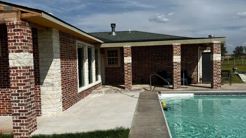 Brick and stone home with a covered patio running alongside a swimming pool