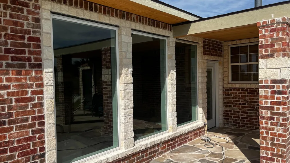 Large picture windows and stone columns above a flagstone patio on a brick home
