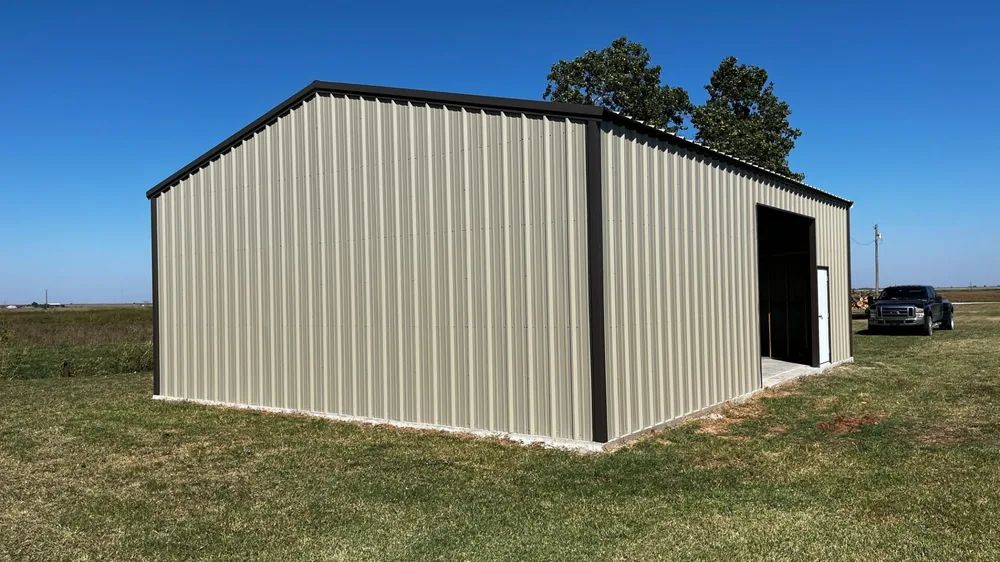 Tan steel garage building with a roll-up door on an open grassy lot