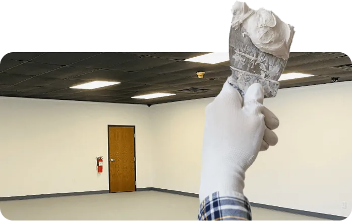 Gloved hand holding a loaded taping knife in front of a finished, freshly painted room