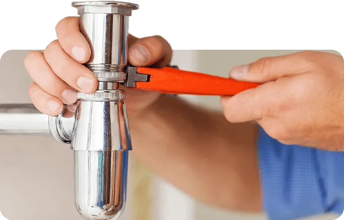 Plumber tightening the chrome P-trap under a sink with a red pipe wrench
