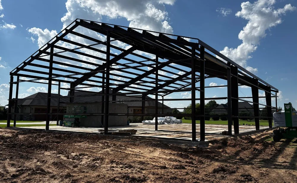 Black steel building frame erected on a slab under a bright cloudy sky