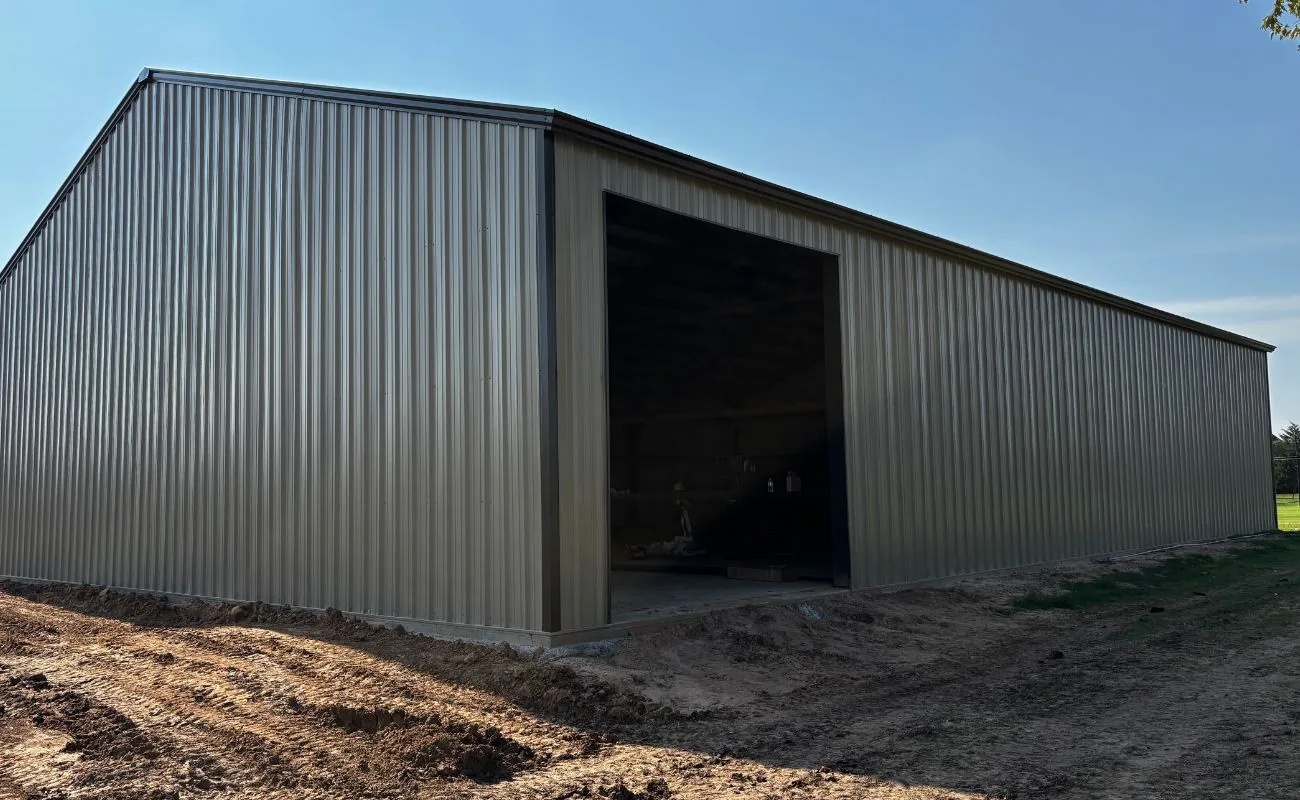 Finished tan steel building with an open bay door on a freshly graded lot