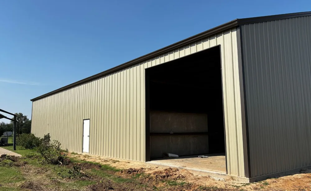 Side wall of a tan metal shop building with a walk door and an open bay